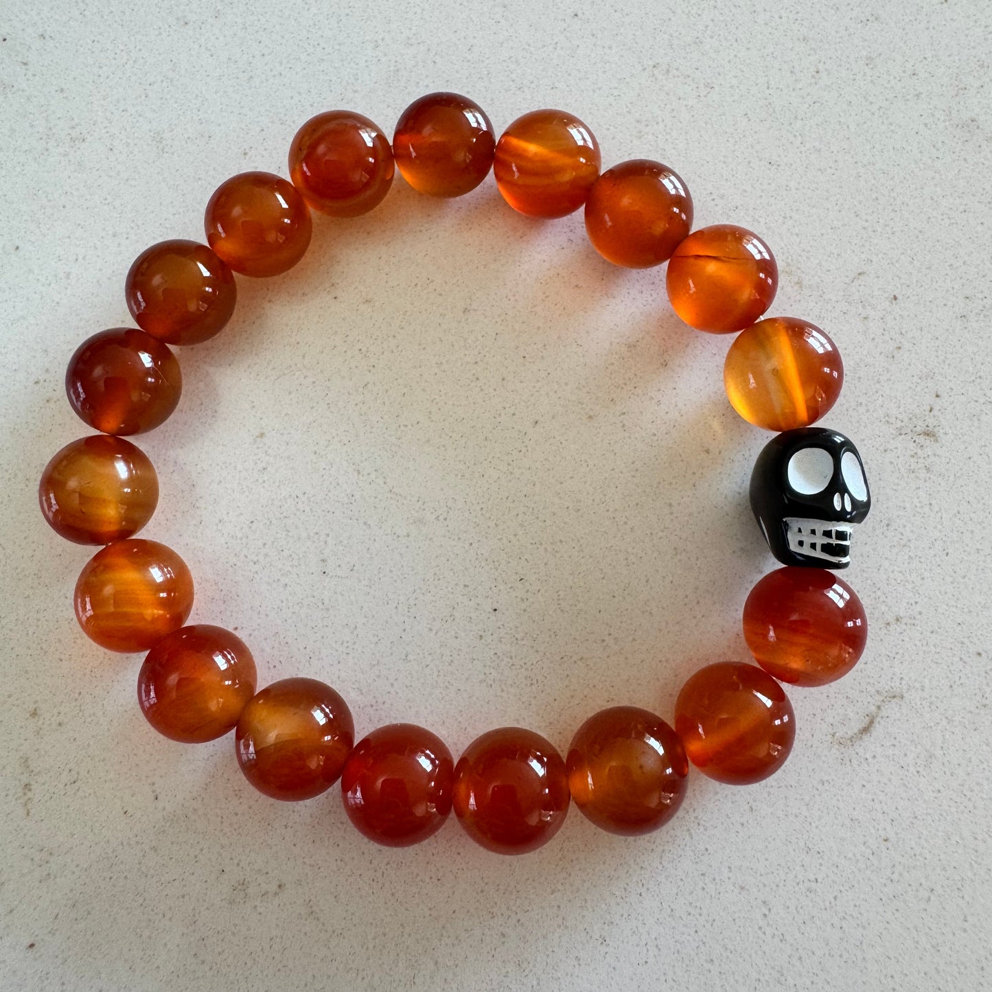 Bracelet with orange beads and a black and white skull charm on a light gray background